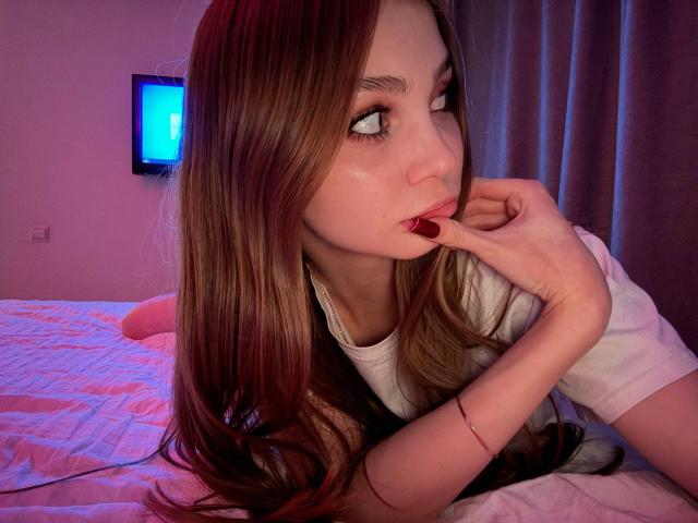 Foto van Calista Swiatek met lang bruin haar, liggend op een bed, hand in de buurt van de mond, die met een verleidelijke blik naar de zijkant kijkt. uitdrukking.
wit T-shirt, rode nagels, paars en blauw licht, gordijnen op de achtergrond..