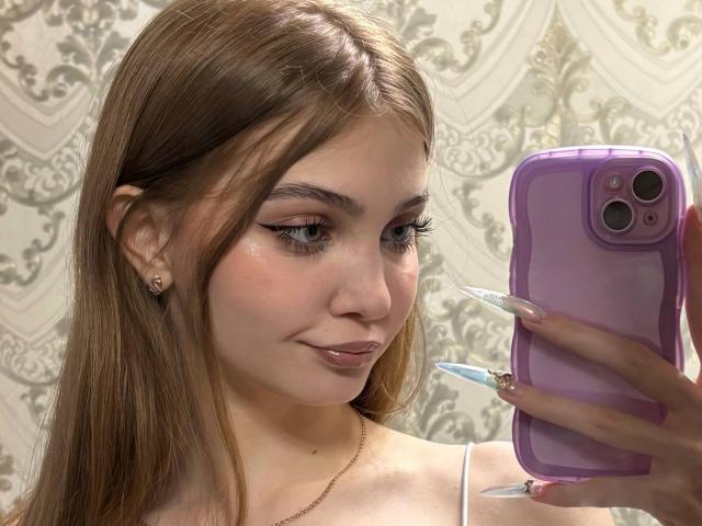 Fotografia ravvicinata di Calista Swiatek, una giovane donna con lunghi capelli castani, che tiene in mano un iPhone viola con la mano destra. caratterizzate da unghie lunghe, appuntite e dipinte di blu. Ha un sorriso appena accennato..