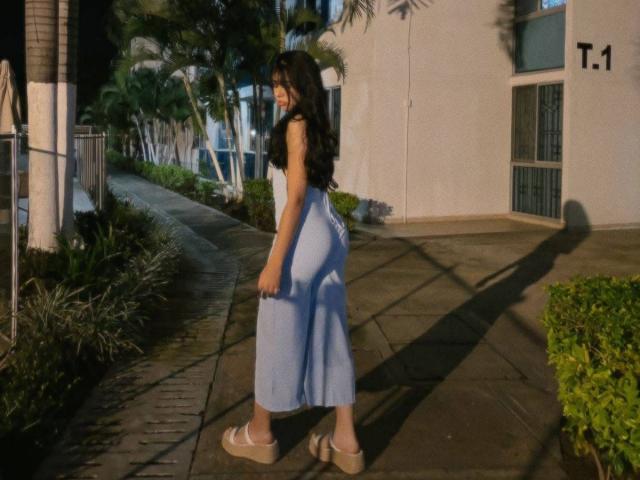 MiluSky stands on a sunlit sidewalk, back to the camera, wearing a black sleeveless top and light blue skirt that accentuates her curvy ass. She's in sandals, casting a long shadow.