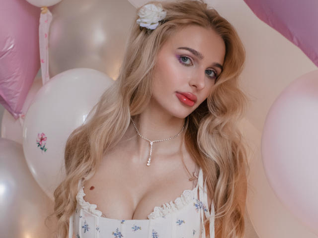 Flora Davis, una donna bionda con lunghi capelli ondulati, indossa un abito bianco con fiori e bordi in pizzo, e un fiore bianco tra i capelli. accessorio, circondato da palloncini rosa e bianchi. Molto attraente..