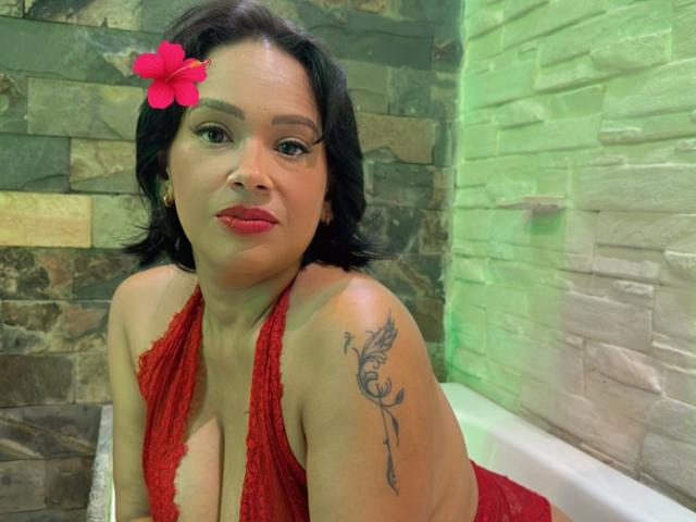 LoraineClof, con cabello oscuro, una flor roja en el cabello, un top halter rojo, escote pronunciado, tatuaje en el hombro derecho, verde y muro de piedra marrón, fondo iluminado en verde, expresión seductora, sexy, ambiente de jacuzzi..