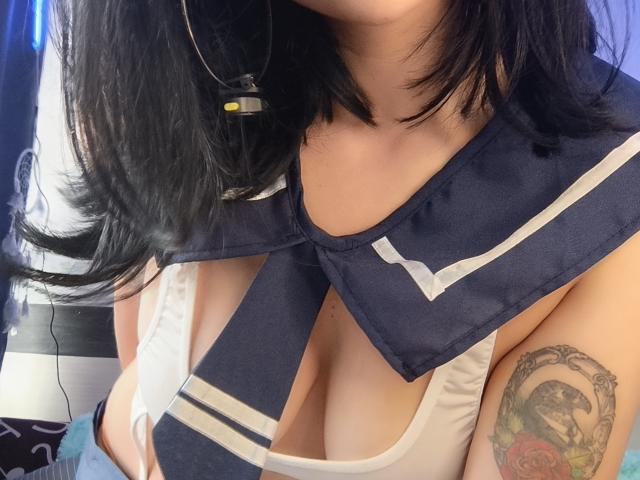 Primo piano di CandyParis con i capelli neri, che indossa una maglia da marina blu scuro con strisce bianche, che lascia intravedere il décolleté. Tatuaggio visibile di una donna con rose sulla parte superiore del braccio. Aspetto carnoso e sensuale..