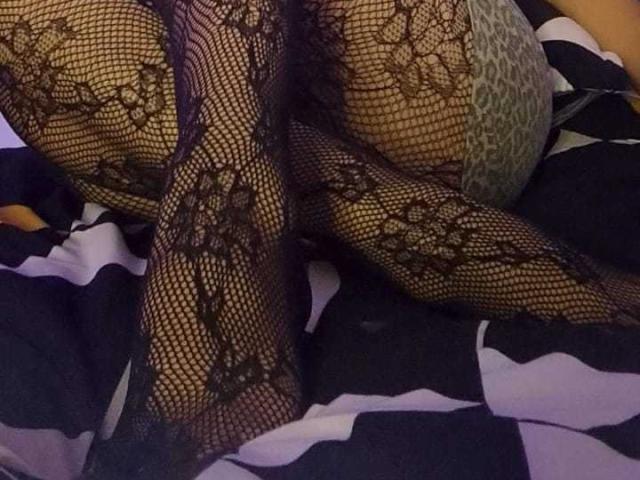 Primer plano de las piernas de ScarletteThoms cruzadas, vistiendo medias de encaje negro con estampado de rejilla, mostrando intrincados patrones florales. ScarletteThoms también lleva ropa interior con estampado de leopardo. La colcha de cama, con un estampado en blanco y negro, está debajo. Increíblemente atractivo/a..