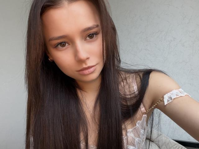 Primo piano di Elenore Baksh, una giovane donna con lunghi capelli neri lisci, occhi marrone chiaro e un'espressione seria. Indossa una camicetta bianca in pizzo con spalline che scendono dalle spalle, e guarda direttamente l'obiettivo..