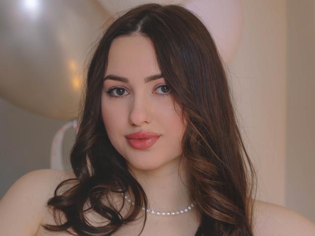 Close-up van ChristinaBliss, een mollige vrouw met lang, golvend bruin haar, die een parelketting draagt en rode lippenstift heeft. Ze heeft grote, uitdrukkingsvolle ogen en een lichte glimlach, en straalt een zekere seksuele aantrekkingskracht uit..