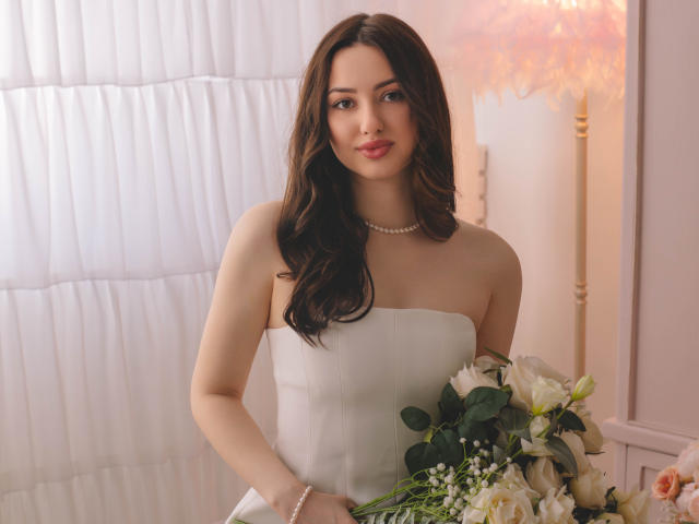 Fotografia de ChristinaBliss, uma mulher curvilínea com cabelos longos e pretos, vestindo um vestido de noiva branco sem alças, segurando um buquê de flores brancas e verdes. Iluminação suave, tensão erótica sutil..