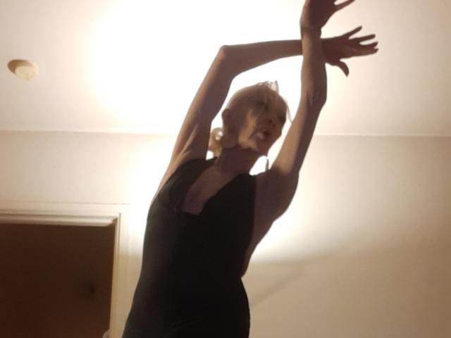 Silhouette of IssahneMay, arms raised, wearing a black dress, standing in front of a bright window, creating a dramatic light and shadow effect. Fucking intense, shadowy, erotic vibe.
