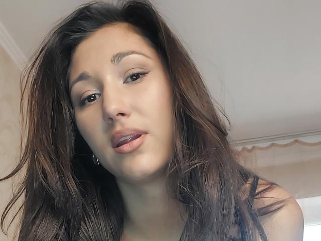 Fotografía de primer plano de LindaErnestine, una joven con cabello largo y castaño oscuro, labios ligeramente entreabiertos y una mirada seductora. expresión. Su mirada está dirigida a la cámara con un ligero toque de tensión sexual..