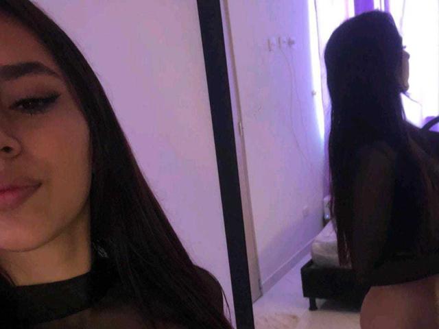 Fotografia di SiennaLanne, che mostra metà del suo viso con capelli scuri e trucco occhi smokey, e la sua schiena con lunghi capelli, in una una stanza scarsamente illuminata, indossa una maglietta nera. Incredibilmente attraente..