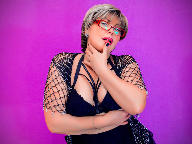 Opera d'arte digitale di LonelyMonika, con capelli corti grigi, occhiali rossi e una maglia a rete nera. Lei si sta toccando il collo, mostrando il décolleté. Sfondo rosa-viola acceso. Dettagli luminosi al neon sugli occhiali.