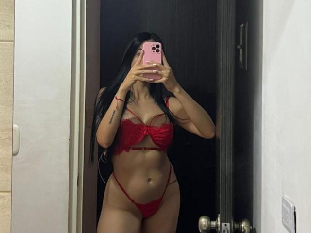 IsabellaJames, with long black hair, stands in front of a mirror, taking a selfie with a pink phone. She's wearing red lace lingerie, her hand partially covering her face. Her stomach is exposed.