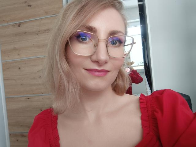 CinderellaMoon, close-up foto, draagt een rode jurk met pofmouwen, gouden montuurbril, blond haar tot op de schouders. paarse oogschaduw, lichte huid, subtiele glimlach, houten wand als achtergrond, heldere lichtbron. Heel schattig.