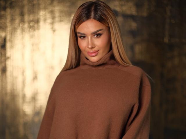 EvaZane, langes, braunes Haar, brauner Rollkragenpullover, weiches, indirektes Licht, leichtes Lächeln, strahlende Haut, leichte Schatten. warme Farben, sexy, selbstbewusst, entspannte Pose, subtile Anspannung, attraktiv, lässiger Stil.