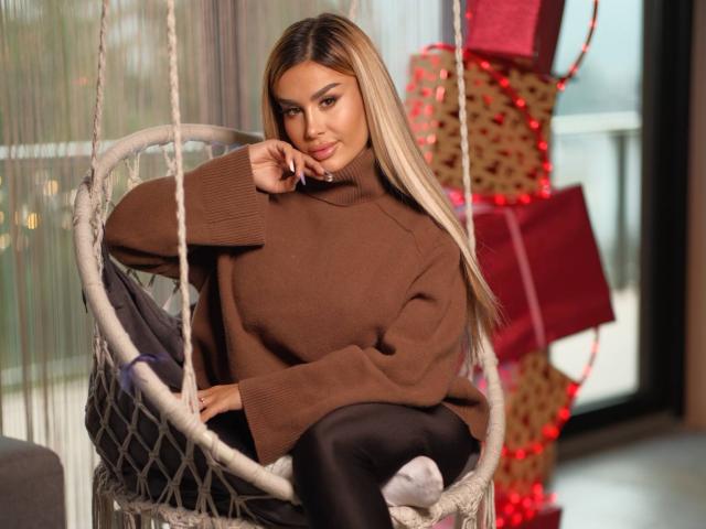 EvaZane, cheveux longs, pull marron, pantalon noir, assise sur une balançoire blanche, main près du visage, sourire séduisant, arrière-plan. avec des cadeaux rouges flous, une lumière vive, une pose décontractée, sexy, détendue, un regard direct..