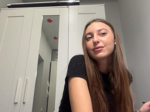 ErinMarrujo heeft lang bruin haar, een lichte huid en draagt een zwarte top. Ze glimlacht met haar hoofd iets scheef en laat kleine, schattige borsten en een aantrekkelijk gezicht zien..