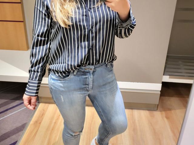 Linnea-hot with a striped black and white shirt, blue ripped jeans, and blonde hair, holding a phone in a mirror selfie, showing her ass and slightly visible tits.