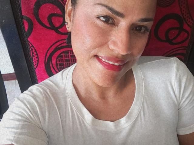 IvannaDuran with medium skin, brown eyes, and red lipstick, wearing a white shirt, smiling, showing her face and upper chest, with short brown hair, small earrings.