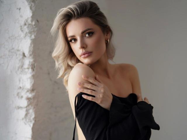 MoonX-hot with blonde hair, covering her tits with a black shirt, looking seductively at the camera, gray eyes, subtle makeup, soft light, wavy hair, small gold earrings.