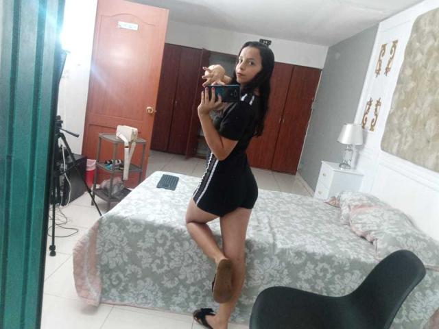 NicolleJane stands in a room, taking a mirror selfie. She's wearing a black shirt and shorts, showing her ass and holding a small dog. She's also in high heels.