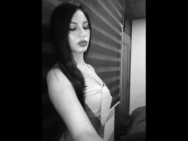 Black-and-white photo of IsabellaSex69 with long dark hair, closed eyes, and full lips. She's wearing a strapless top, showing her tits, and has a small nose piercing.