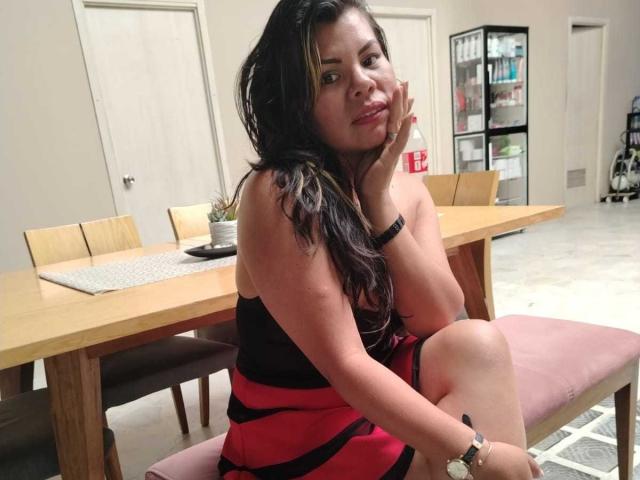 KiaraXMoon, with long black hair and a small butt, sits on a pink bench, wearing a black and red dress, resting her head on her hand, looking cute.