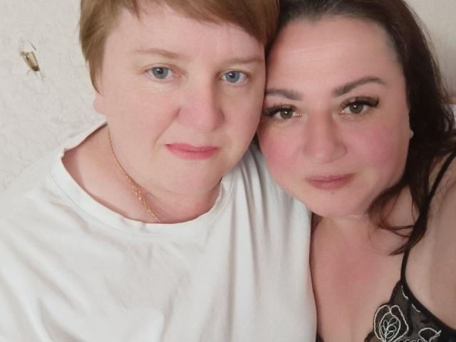 MollyAndJane with short red hair and pale skin, wearing a white shirt, stands next to MollyAndJane with brown hair and pale skin, wearing a black floral top.