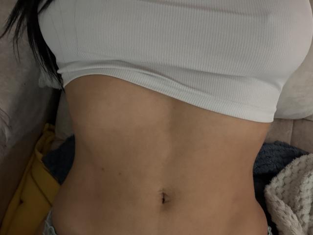 NicoColeman's flat, toned stomach with a small navel in the center, wearing a white ribbed crop top, revealing her lower abs. Her skin is light brown.