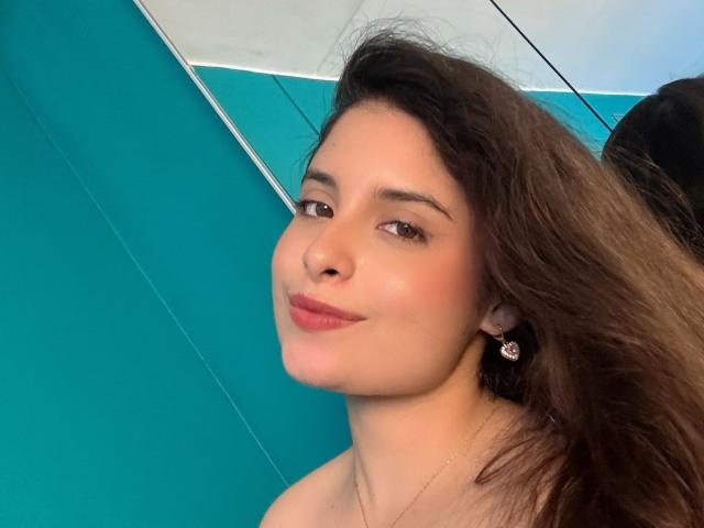 Luciana Blake tiene el pelo castaño, una cara bonita y está sonriendo con labios rosados. Lleva un arete pequeño y un collar. Sus senos no son visibles..