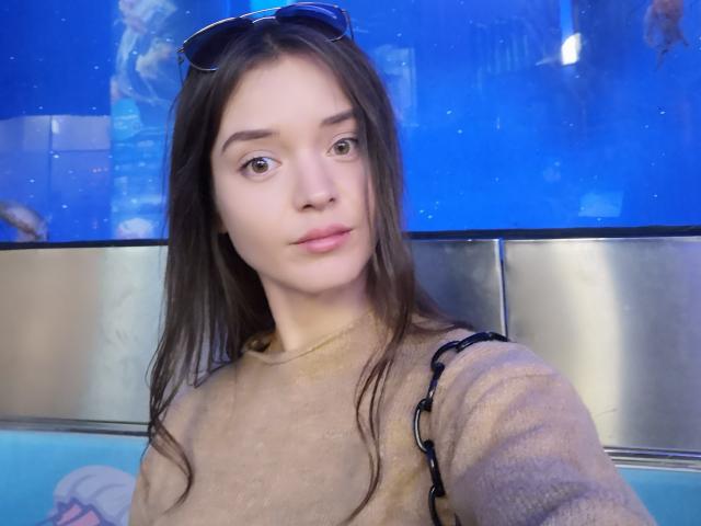 SonyaLovelace has long brown hair, blue eyes, and light skin. She wears a beige sweater with black straps, and sunglasses rest on her head. She has small, perky tits.