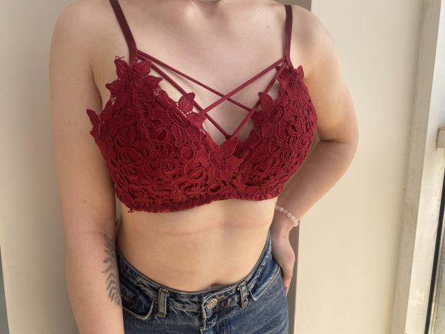 Il reggiseno rosso in pizzo di Steisii, con dettagli a spallina che mette in mostra il seno, abbinato a jeans blu, in posa con una mano sul fianco, ha un tatuaggio sul braccio destro..