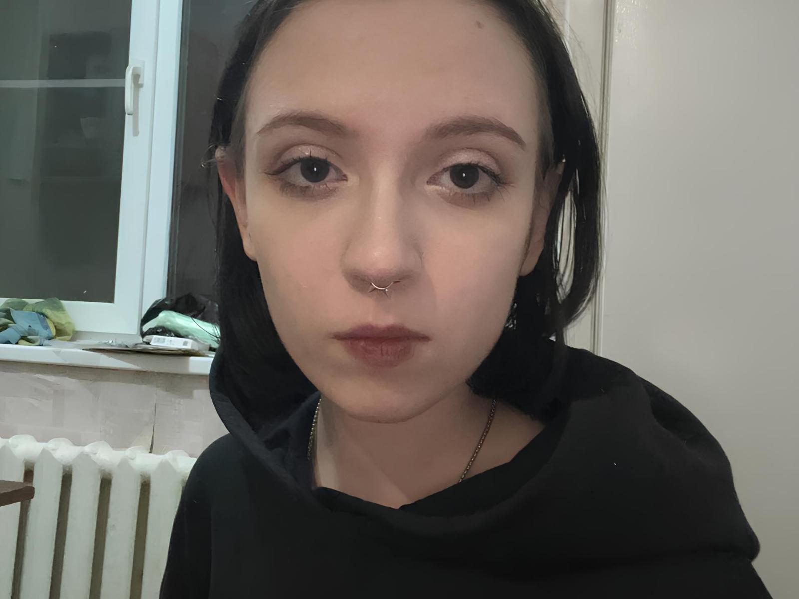RosioVardaro has pale skin, black hair, a nose ring, and wears a black hoodie. She's looking straight at the camera with slightly pouty lips. Her tits are not visible.