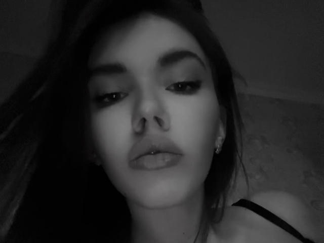 Black-and-white selfie of JuanaGoldmann with dark hair, arched eyebrows, subtle eyeliner, and small earrings, showing a slightly open mouth and a soft, relaxed expression.