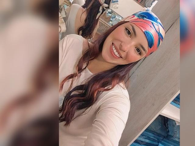 MartinaRey with long wavy brown hair, smiling, wearing a white long-sleeve shirt and a blue, red, and pink patterned headband, in a selfie.