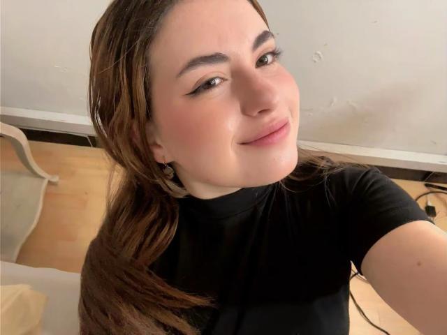 VicluX has light skin, brown eyes, and long brown hair, wearing a black shirt, smiling slightly with a cute face, and small earrings visible.