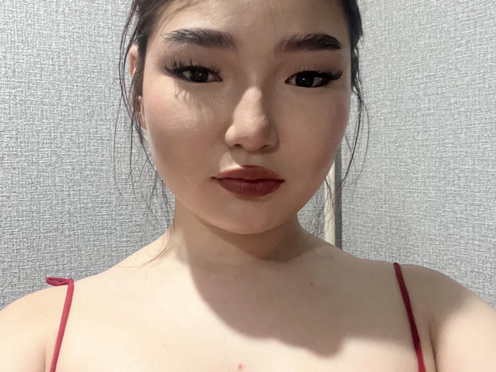 WilliemaeWainio with dark, arched eyebrows, long eyelashes, red lipstick, and red spaghetti straps, looking directly at the camera, pale skin, and a subtle shadow on the right side.