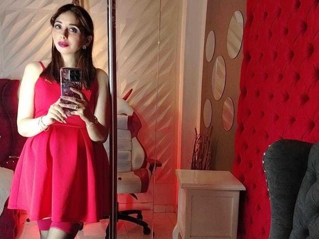 StephanieSun in a red dress, holding a phone, standing in front of a mirror, showing her tits and ass, with pink lipstick and brown hair.