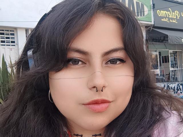 LilithHeavy has wavy dark brown hair, a nose ring, and black eyeliner. She's wearing headphones and has pink lipstick. Her ass is not visible.