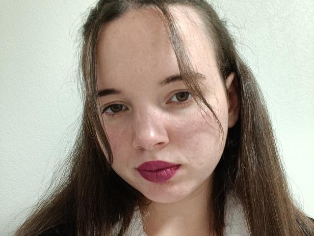 Jaklinna's face, pale skin, brown eyes, long brown hair, slight blemishes, pinkish-purple lipstick, white background, casual expression. Boobs not visible, focus on face.