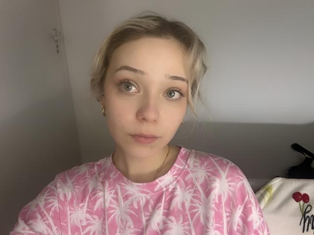 Donita Dunn mit blonden Haaren, grünen Augen und einem pinkfarbenen T-Shirt mit Palmenmotiv, die leicht zur Seite schaut, mit goldenen Ohrringen und einer dezenten goldenen Halskette, mit einem neutralen Gesichtsausdruck..