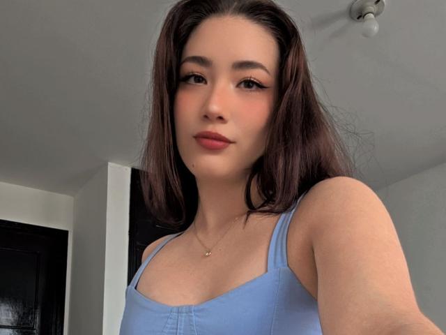 Stardustt with long brown hair, blue tank top, and a gold necklace, has a cute face, small tits, and a subtle smile, looking at the camera.