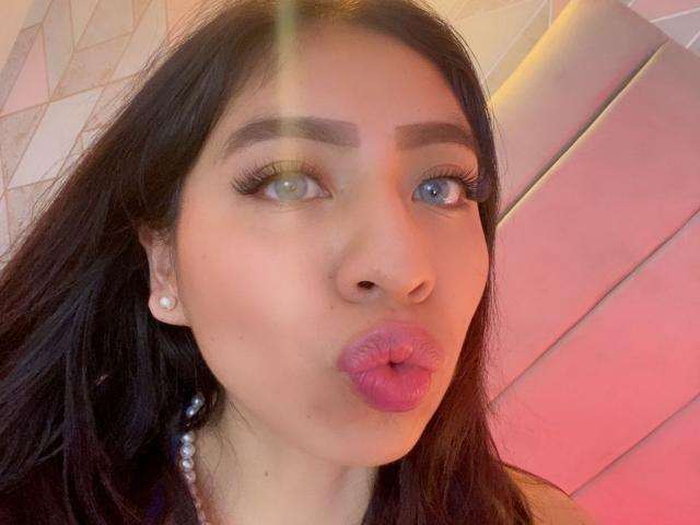 ZoeRedds with heterochromia, pouty pink lips, dark straight hair, pearl earrings, blue eye, green eye, subtle makeup, and a soft glow on her face.