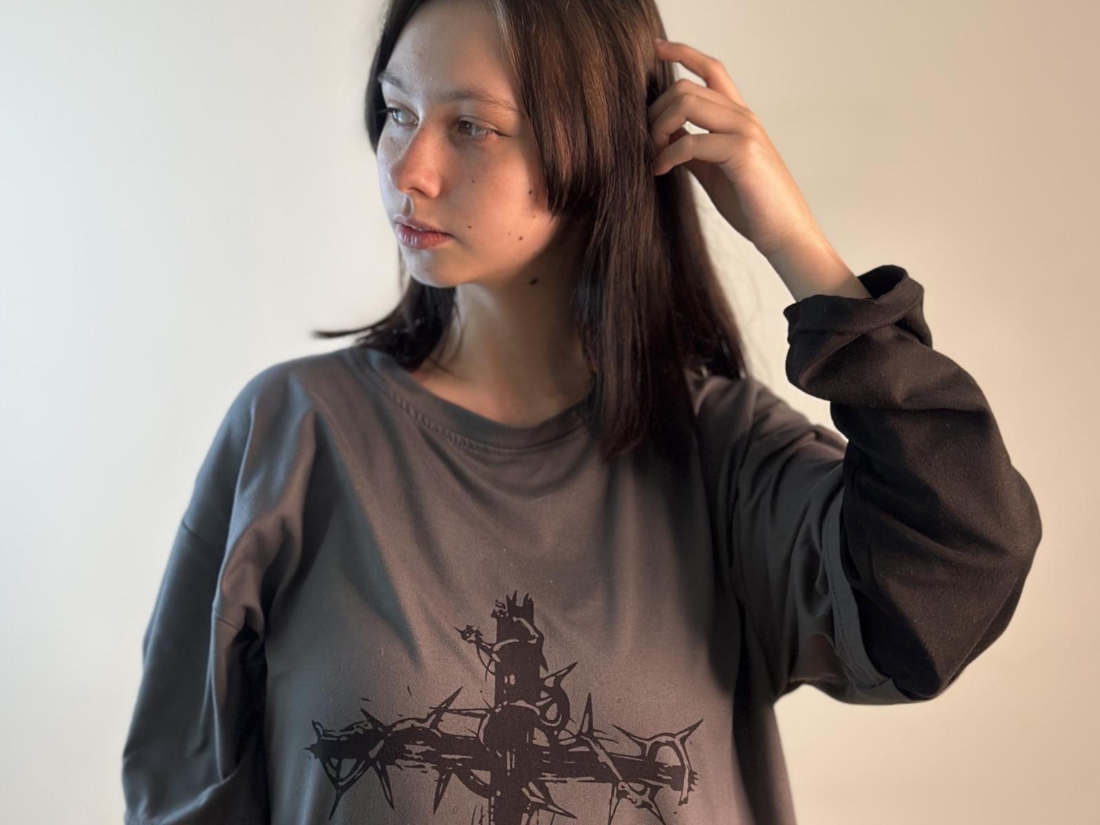 AnnamaeGenito with long brown hair, wearing a gray sweatshirt with a black graphic, hand in hair, looking to the side, soft light on her face.