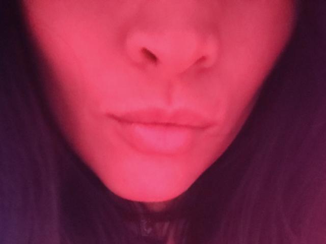 IssisDiosa's pink-tinged face, focusing on her slightly parted lips and nose, with dark hair framing her face. Soft, blurry, and sensual.