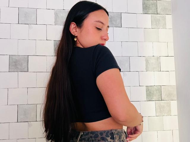 RosalieDupont with long black hair, wearing a black crop top, showing her back, and leopard print pants, looking over her shoulder with a small gold earring.