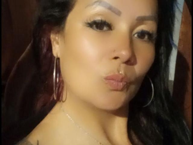 CelesteLaurent with puffy lips, hoop earrings, and long black hair, has a nose ring and is making a pouty face, showing her shiny, smooth brown skin.