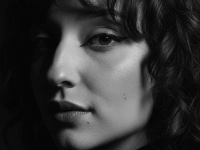 Black and white photo of NickiCandy's face showing her wavy hair, eyeliner, and small moles on her cheek and lower lip. Her expression is slightly pouty.