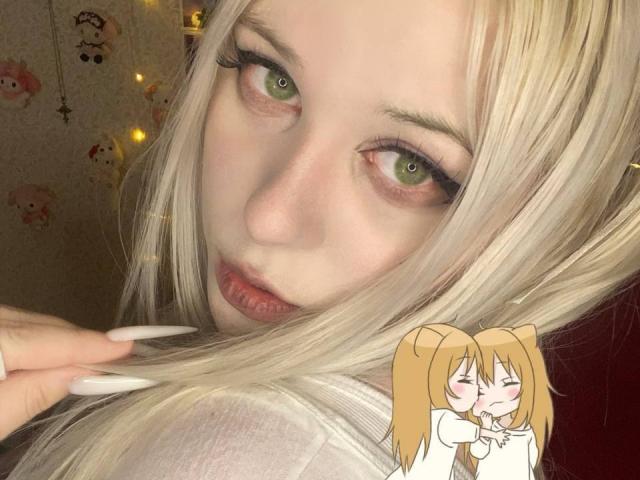 TinaEvanss has blonde hair, green eyes, and long white nails. She's looking seductively at the camera with her lips slightly parted. Chibi TinaEvanss in the bottom right.