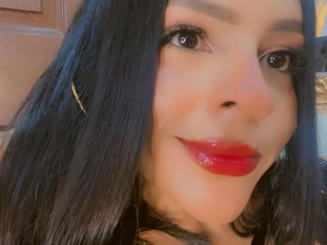 LindaFrancoo's face with glossy red lipstick, black straight hair, brown eyebrows, and gold earrings. She's smiling slightly with visible eyelashes and a warm skin tone.