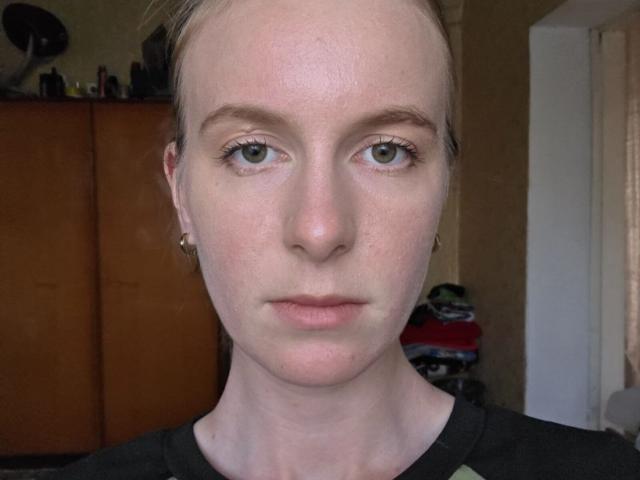 DebbyPennimpede has pale skin, blue eyes, and a serious expression. She's wearing a black shirt with small earrings. Her blonde hair is pulled back.