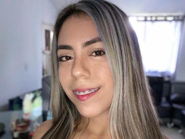 QuickHookup has long, straight, blonde-highlighted hair, brown eyes, and a cute smile showing metal braces. Her tan skin looks smooth, and she's wearing pink lipstick.